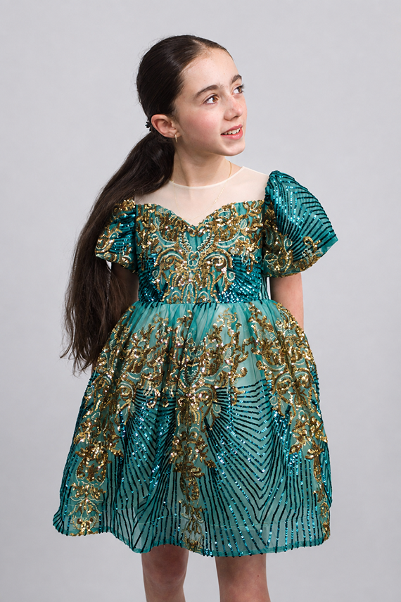 Girl wearing the KoKo Zafira emerald-green and gold Baroque sequin party dress with puff sleeves, an illusion neckline and a full layered skirt.