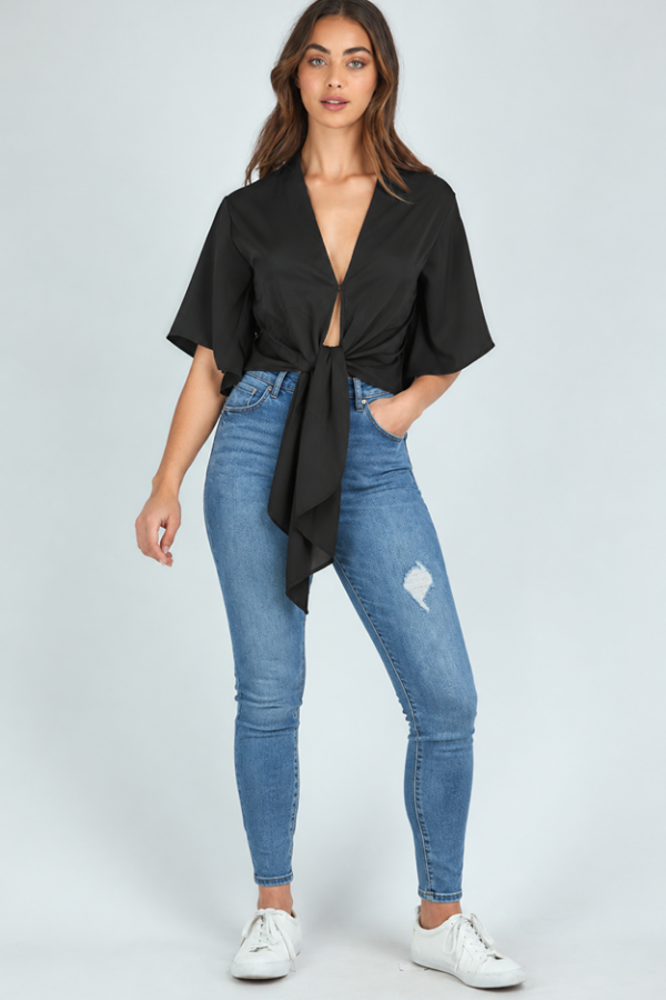 Model wearing the KoKo Elara black tie-front top with loose kimono-style sleeves and long draping ties, paired with white pants.